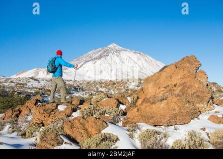 Mature man walking in Teide national park on Tenerife with mount Teide, the highest mountain in Spain, capped in snow in background. Canary Islands. Stock Photo