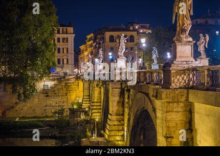 Old Roman Stone Bridge With Angel Statues River And Historic Buildings Illuminated At Night. Stock Photo