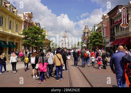 Standing on a street of a theme park in middle of a crowd of people. Walking visitors in theme park in front of a cute castle with cityscape. Paris Fr Stock Photo