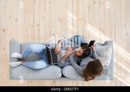 Top view of family sitting on couch, using laptop, phone Stock Photo