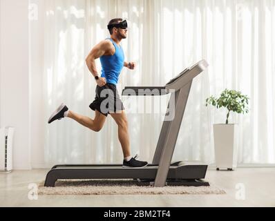 Full length profile shot of a young man running on a treadmill and wearing a vr headset at home Stock Photo