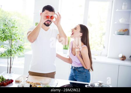 Portrait of two people married chef prepare veggie salad dish dinner man hold cherry tomato close hide cover eyes face woman look laugh comic in Stock Photo