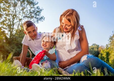 Mother's day. Happy family spending time outdoors sittting on grass in park. Mom with two children son daughter smiling. Stock Photo