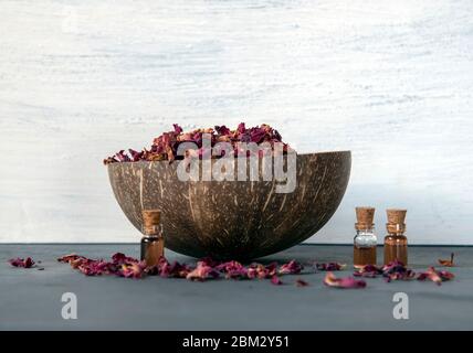 A coconut bowl filled with dried rose petals and several glass bottles of rose oil . Stock Photo