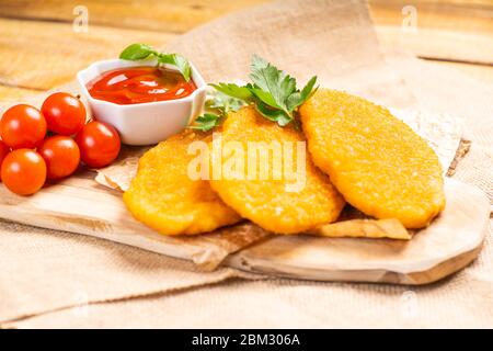 Fast homemade food.Fast food.Chicken breaded schnitzels on a wooden kitchen board with ketchup and basil leaves and tomatoes on a wooden background. Stock Photo