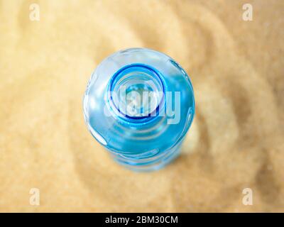 Open blue plastic bottle with drinking water on a yellow sea sand. Concept of thirst, hot summer weather, sea holiday and vacation on a beach. Stock Photo