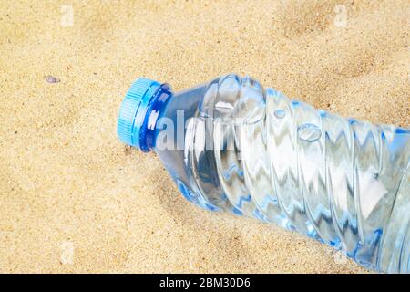 Blue plastic bottle with drinking water on a yellow sea sand. Concept of thirst, hot summer weather, sea holiday and vacation on a beach. Top view. Stock Photo