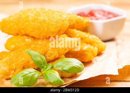 Fast homemade food.Fast food.Chicken breaded nuggets with basil leaves and ketchup on a wooden kitchen board on a wooden table . Stock Photo