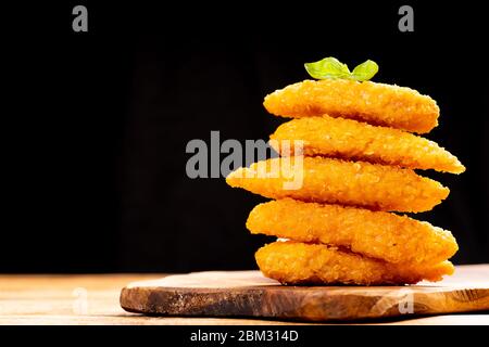 Fast homemade food.Fast food.Chicken breaded nuggets with basil leaves on a wooden kitchen board on a wooden table on a black background. Stock Photo