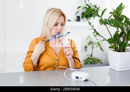 woman makes inhalation nebulizer at home. holding a mask nebulizer inhaling fumes spray the medication into your lungs sick patient. self-treatment of Stock Photo