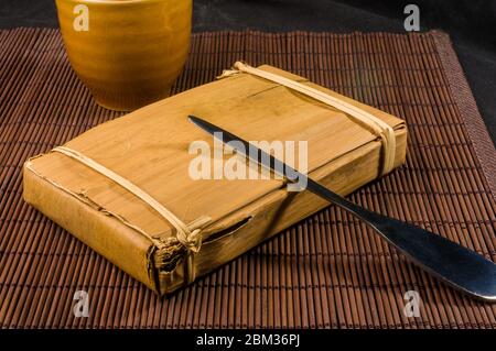 Chinese pressed PU-erh tea in bamboo leaf packaging and tea knife, close-up Stock Photo
