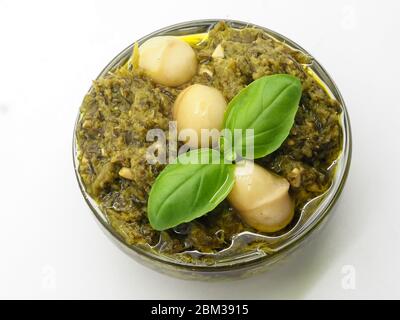 A Bowl Of Green Pesto Sauce, Topped With Macadamia Nuts And Basil Leaves, On A White Background, London, UK Stock Photo