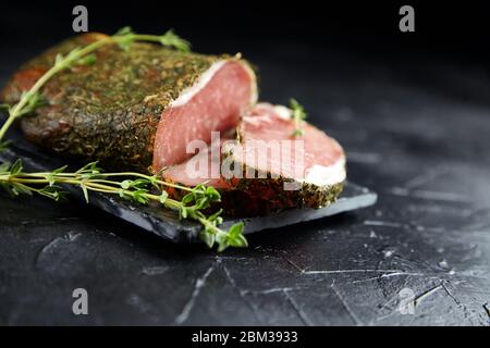 Dried pork, polendwitz, jerky tenderloin, fresh green thyme, slate cutting board on black background. Cured pork meat. Polenitsa is a dry-cured filet. Stock Photo