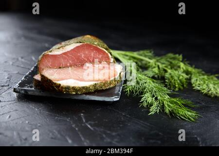 Gerky pork with spices, fresh green dill, slate cutting board on black stone table. Polendwitz is a jerky tenderloin. Sun-dried filet, selective focus Stock Photo