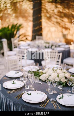 Wedding dinner table reception. Round banquet tables for guests with gray tablecloth. Floral arrangement of roses in center of the table. Garland on Stock Photo