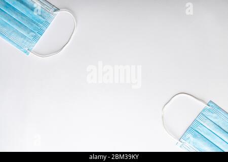 Several medical blue disposable protective masks lying one opposite the other on a white background. A surgical dressing closes the mouth and nose Stock Photo