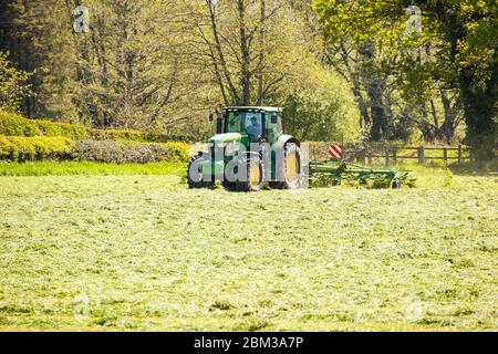 Farmer driving tractor turning grass to dry before gathering it for silage in Cheshire farmland countryside England UK Stock Photo