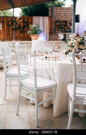 Wedding dinner table reception. A close-up of the white classical chair for Chiawari's wedding, Tiffany near the round table, amid the lights of the Stock Photo