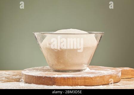 Dough in glass bowl on wooden cutting board. Close up. Stock Photo