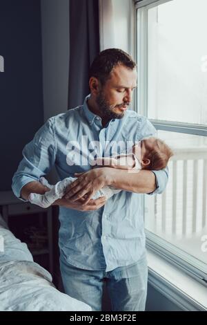 Middle age Caucasian father trying to calm down newborn baby. Man parent holding rocking child on his hands. Authentic lifestyle family moment. Single Stock Photo