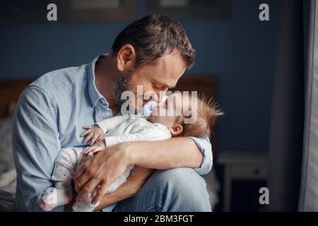 Middle age Caucasian father kissing sleeping newborn baby girl. Parent holding rocking child daughter son in hands. Authentic lifestyle parenting fath Stock Photo