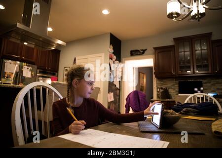 Blonde Girl at Kitchen Table Does School Work on Tablet Computer Stock Photo