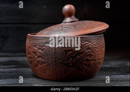 brown clay pan on a black wooden background with authentic carvings Stock Photo