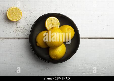 Yellow lemons in a black bowl, on a white wooden table Stock Photo