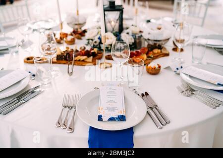 Wedding dinner table reception. White plate on the table, three forks on the left, three knives on the right. The wedding menu is in the plate. Top Stock Photo