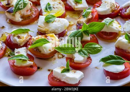 Tomatoes with Mozzarella cheese and Basil (Caprese) arranged on a plate drizzled with Olive Oil and Balsamico dressing Stock Photo