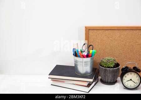 Copy space. Workplace office worker. Alarm clock, succulent in ceramic pot, writing board, bucket with scissors, felt-tip pens, ruler, three notebooks Stock Photo