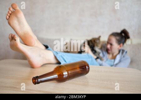 A drunk girl sits on a sofa and plays with a cat with a bottle in focus. Close up. Stock Photo