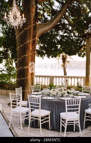Wedding dinner table reception. Round banquet tables for guests with gray tablecloth. Floral arrangement of roses in center of the table. Garland on Stock Photo