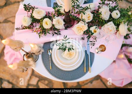 Close-up of plates, cutlery, wine glasses on table. Decorating dinner for two by candlelight. Floral arrangement of roses in the center of table Stock Photo