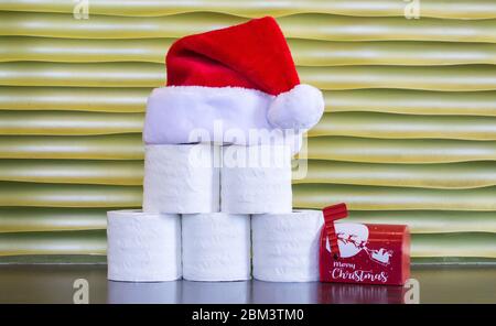 rolls of toilet paper with a red and white Santa Claus hat on top, next to a small Christmas mailbox ,against a gold background with copy space Stock Photo