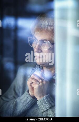 Elderly woman behind window looking out with concern. Stock Photo