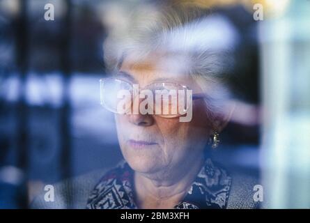 Elderly woman behind window looking out with concern. Stock Photo