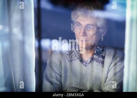 Elderly woman behind window looking out with concern. Stock Photo