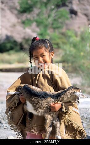Smiling young Indigenous girl with kid goat in Purmamarca, Jujuy, Argentina Stock Photo