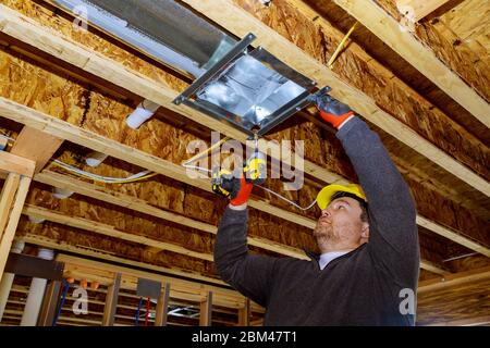 Male technician mounted air heating and cooling system on ceiling steel roof structure ventilation system Stock Photo