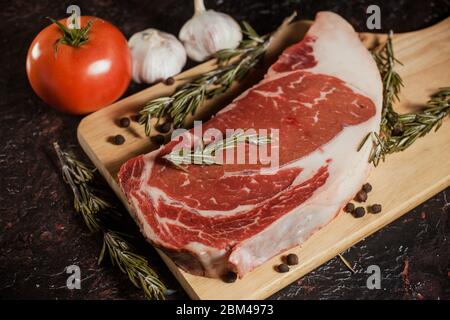Raw ribeye steak with a sprig of rosemary, garlic and tomatoes