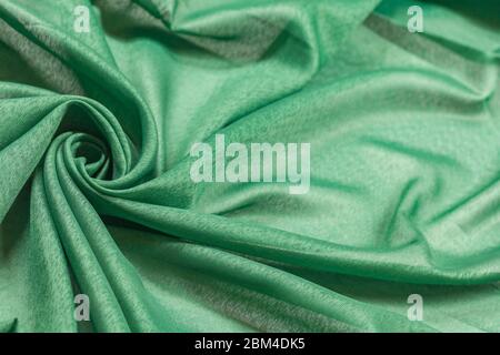 Creased green curved cloth material fragment with swirl as fabric background texture Stock Photo
