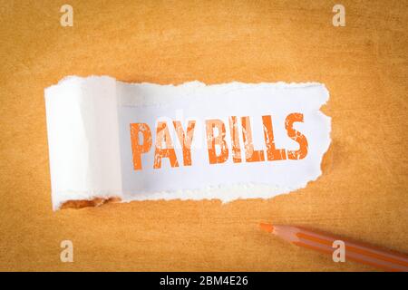 PAY BILLS concept. Text under torn paper. Orange pencil and office supplies on an paper background Stock Photo
