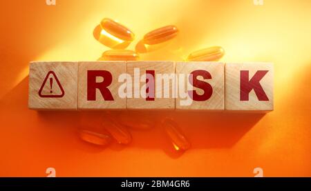 Risk Word on Wooden Cubes and oil capsules pills around on orange background. Medical healthcare concept Stock Photo
