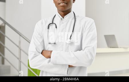 Crop of unrecognizable professional therapist with stethoscope on neck posing with arms crossed. Portrait of smiling african male doctor in white lab Stock Photo