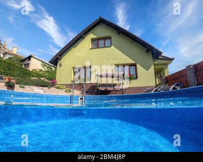 small home swimming pool with two black sun loungers and rocking bench. Underwater split screen view. Covid 19 - Summer 2020 holiday concept. Vacation Stock Photo