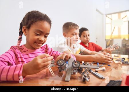 Building kit with colorful pieces for group of three multiracial kids creating toys, having positive emotions. Close up of smiling african girl working on project. Concept of science engineering. Stock Photo