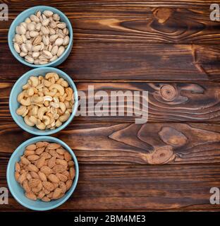 Different types of nuts in bowls on wooden background. Almonds, pistachios, cashews. Healthy food and snack. Diversity of nuts. Layout Stock Photo
