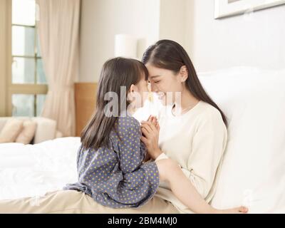loving asian mother and cute daughter sitting in bed at home Stock Photo
