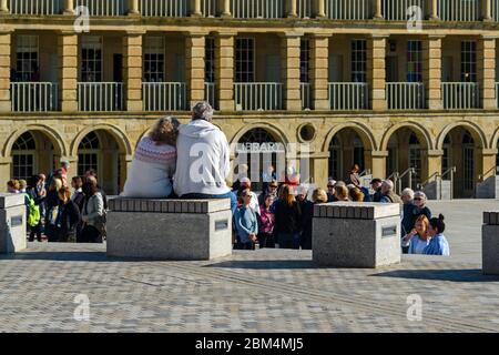 Historic Piece Hall courtyard (sunny piazza, guided tour group, couple sitting close, grand colonnades, arches) - Halifax, West Yorkshire, England UK Stock Photo